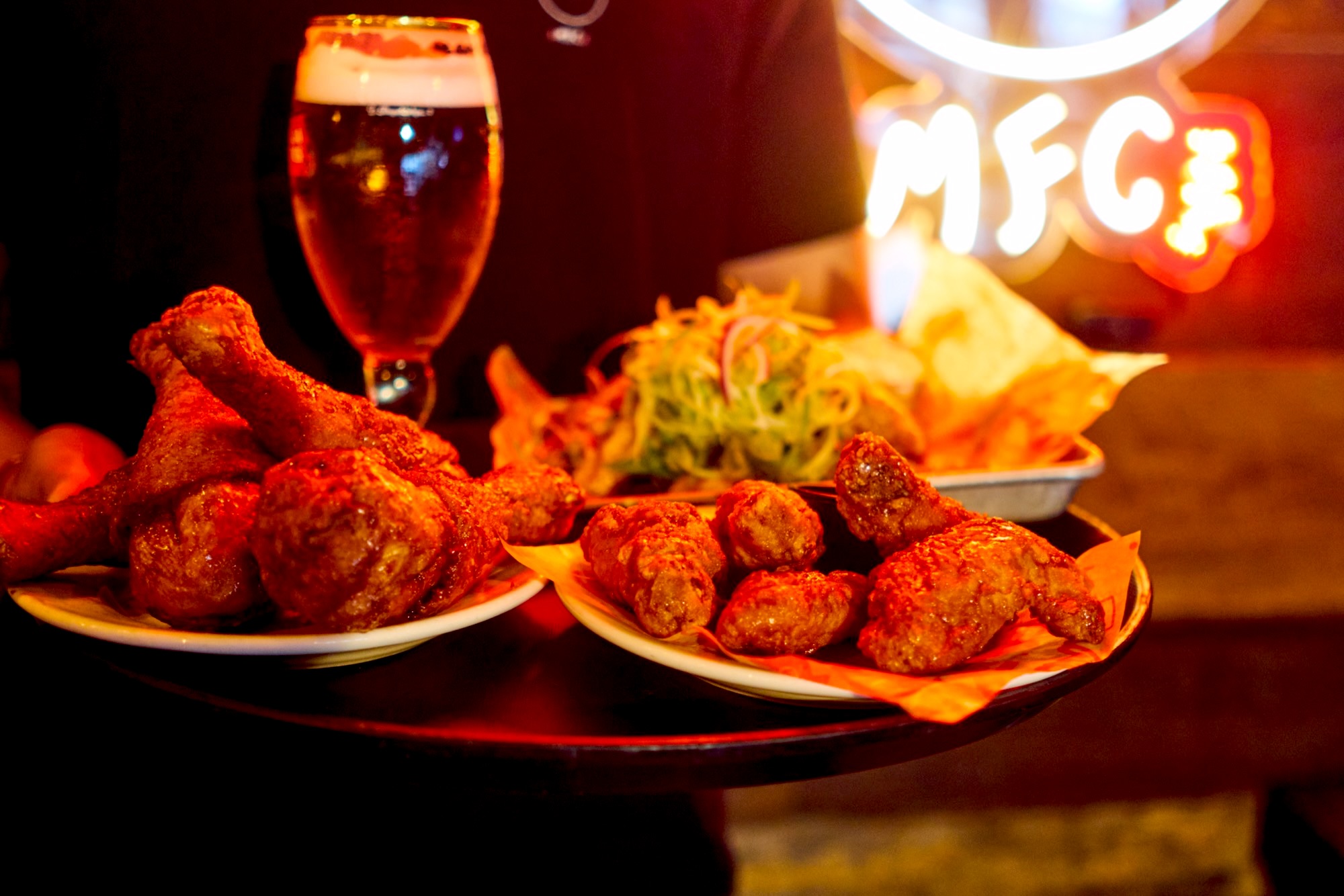 A server carrying fried chicken and a beer past the MFC neon sign
