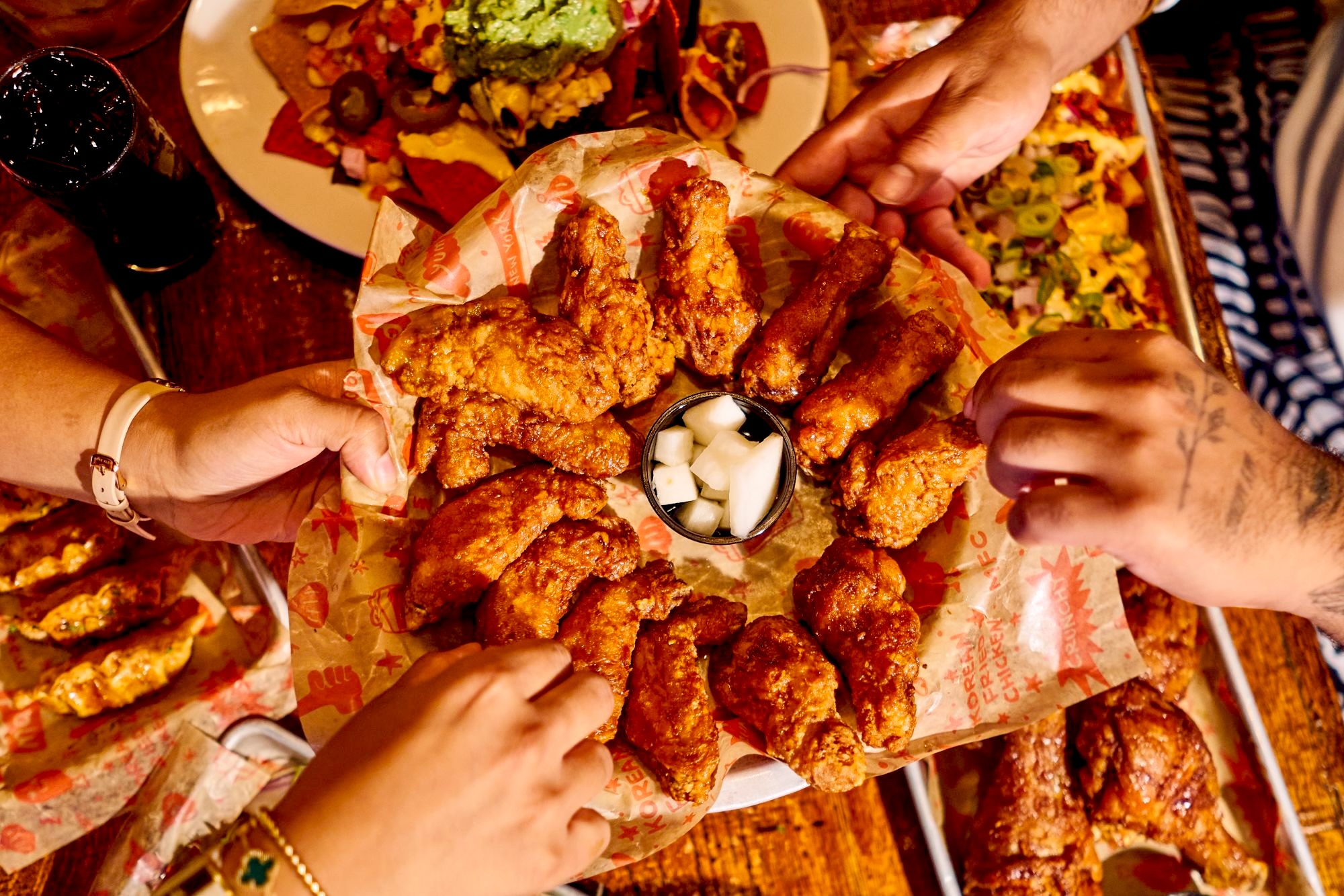 Friends reaching for a platter of Korean fried chicken wings